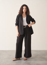 Woman wearing a white tank top and black wide-leg linen trousers against a plain background