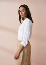 Woman wearing a white fluid crepe button up shirt with pocket details, paired with neutral oatmeal trousers