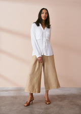 Woman wearing a buttoned up white crepe shirt with pocket details, with cropped neutral wide leg trousers and heels.