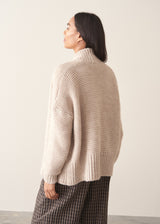 A woman wearing a chunky knit open front cardigan in oatmeal beige with checked barrel leg trousers