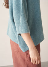 Woman wearing teal knitted sweater and rust red linen trousers