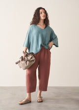 Woman wearing teal knitted sweater and rust red linen trousers