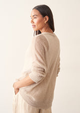 A woman wearing a soft knit cardigan in a light beige colour, worn over a white vest top and paired with matching beige trousers.