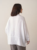 Woman wearing an oversized white linen shirt and checked trousers against a beige background