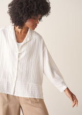 Woman wearing a white striped shirt and beige wide leg trousers against a plain background.