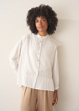 Woman wearing a white striped shirt and beige wide leg trousers against a plain background.