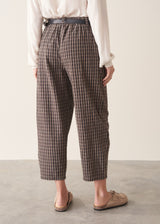 A woman wearing dark brown check barrel leg trousers with a white blouse and matching check jacket