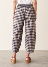 Woman wearing blue and taupe check barrel leg trousers with clog heels and a white t-shirt.