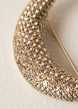 Close up of crystals on a gold crescent moon brooch, on a beige background