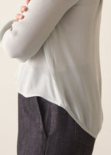 A woman wearing a light blue v-neck blouse with dark jeans against a plain background