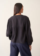 A woman wearing a black embroidered textured cropped jacket over a white top and dark blue jeans.