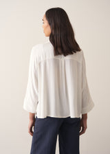 Woman wearing a white blouse and navy pants against a plain background