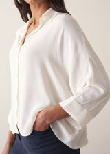 Woman wearing a white blouse and navy pants against a plain background