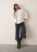 Woman wearing a white blouse and navy pants against a plain background