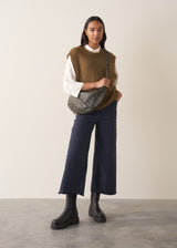 Woman wearing a white blouse and navy pants against a plain background