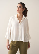 Woman wearing a creamy white blouse and green tapered trousers against a plain background