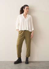Woman wearing a creamy white blouse and green tapered trousers against a plain background