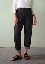 Person wearing dark cotton jeans rolled up against a plain background