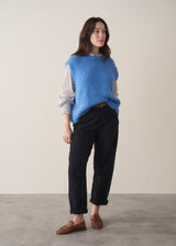 A woman wearing black denim trousers and a white stripe shirt against a beige background