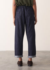 Woman wearing a green sleeveless sweater and dark blue jeans against a plain background