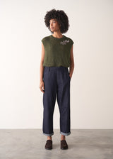 Woman wearing a green sleeveless sweater and dark blue jeans against a plain background