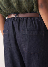 Woman wearing a green sleeveless sweater and dark blue jeans against a plain background