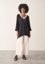 Woman wearing oversized black sweater with off white jeans and black sandals.