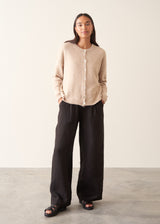 A woman wearing a light beigh knitted cardigan with a white t-shirt and black trousers.
