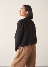 Woman wearing black boxy linen jacket with metal buttons
