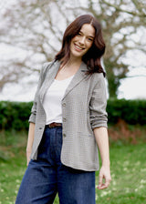 A model stands in front of lush greenery, dressed in a grey seersucker jacket, a white t-shirt and jeans