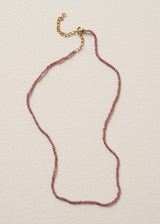 Pink beaded crystal necklace with gold chain, on a beige background