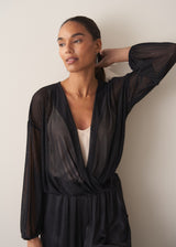 Women wearing a long sleeve sheer sparkle draped top with cream satin camisole and black satin trousers