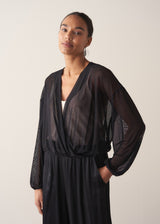 Women wearing a long sleeve sheer sparkle draped top, styled with a cream satin camisole and black trousers