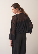 Woman wearing a black sheer top and black wide leg trousers against a plain background