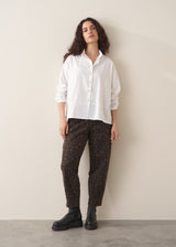 Woman wearing a white shirt and leopard print barrel leg jeans against a plain background