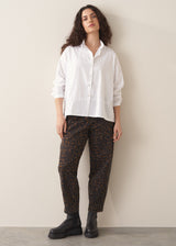 Woman wearing a white shirt and leopard print barrel leg jeans against a plain background