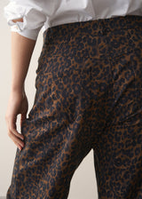 Woman wearing a white shirt and leopard print barrel leg jeans against a plain background