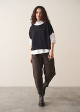 Woman wearing a white shirt and leopard print barrel leg jeans against a plain background