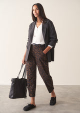 Woman wearing dark brown leopard print barrel leg trousers and a long sleeve white top