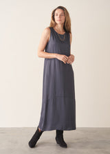 A woman wearing a sleeveless, maxi-length dark blue grey dress with a cocoon skirt
