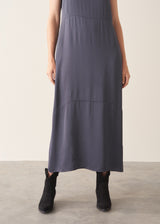 A woman wearing a sleeveless, maxi-length dark blue grey dress with a cocoon skirt