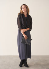 A woman wearing a sleeveless, maxi-length dark blue grey dress with a cocoon skirt