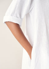 Woman wearing white linen shirt dress with button up detail and pleated from.