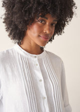 Woman wearing a white linen dress with pintuck detail and mother of pearl buttons against a beige background