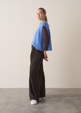 Woman wearing brown, wide leg corduroy trousers and a cornflower blue sleeveless sweater
