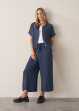 Woman wearing navy blue wide-leg linen trousers with loafers, paired with a matching linen shirt open over a white tee.