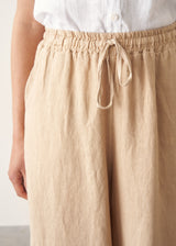 Woman wearing white linen shirt, sand wide leg linen trousers and black sandals