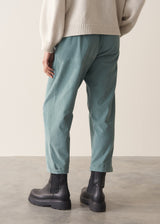 Woman wearing a cream rollneck sweater and aqua cord trousers against a plain background