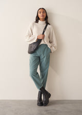 Woman wearing a cream rollneck sweater and aqua cord trousers against a plain background