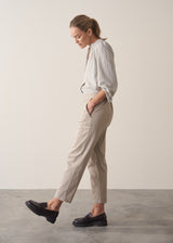 Woman wearing taupe slim fit tapered leg trousers with pale check shirt